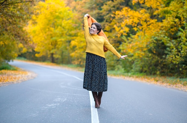 Femme positive ans dans un chandail confortable regarde la caméra le long de la route dans la forêt d'automne o