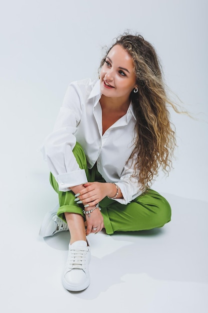 Femme positive aux cheveux bouclés dans une chemise et un pantalon en coton blanc clair sur fond blanc isolé