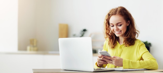 Une femme positive envoie des SMS à des amis en ligne sur son smartphone en pause au bureau assise sur le lieu de travail