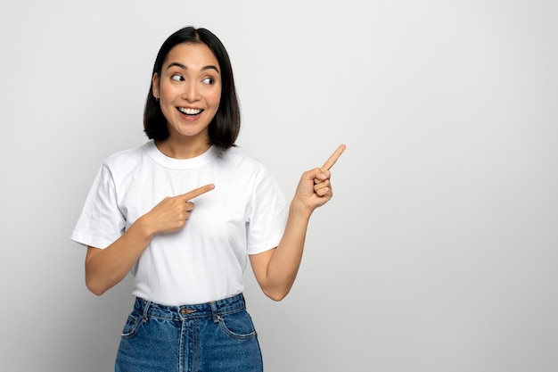 Femme positive joyeuse pointant les doigts loin montrant de l'espace pour votre publicité