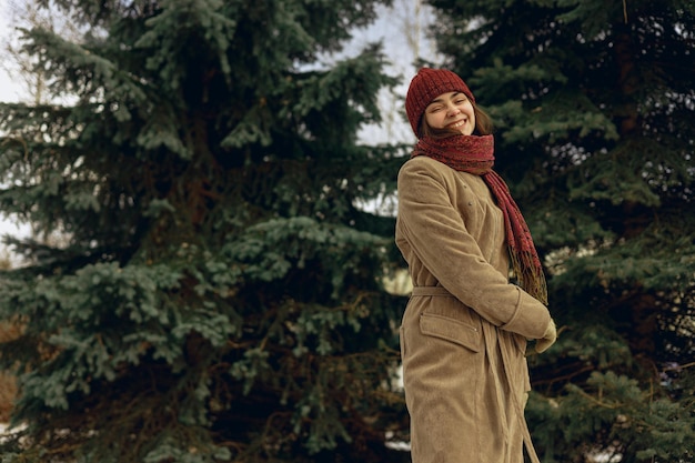 Femme positive portant un manteau chaud et un chapeau avec une écharpe dansant et s'amusant dans le parc d'hiver