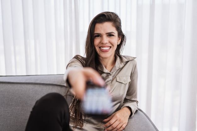 Une femme positive tenant une télécommande sur un canapé.