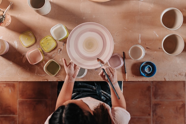 Photo femme potière dans son atelier peignant ses œuvres d'art sur sa table avec différents outils et couleurs assorties