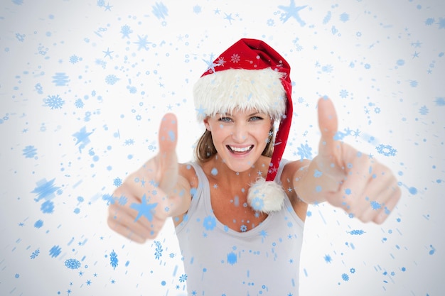 Photo femme avec le pouce levé et un chapeau de noël contre les chutes de neige