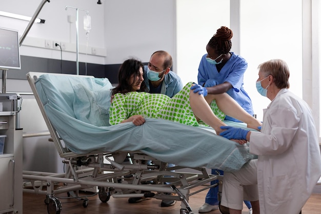 Femme poussant pour donner naissance à un bébé dans la salle d'hôpital, ayant des contractions douloureuses pendant la césarienne. Médecin obstétricien et mari réconfortant une patiente enceinte à la maternité