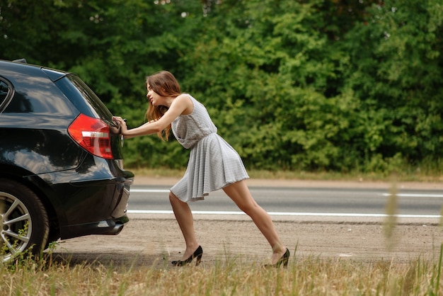 Femme poussant la voiture cassée sur la route, panne