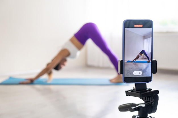 Femme pratiquant des poses de yoga qui s'étend devant la caméra du téléphone blogueur sportif professeur de yoga en ligne