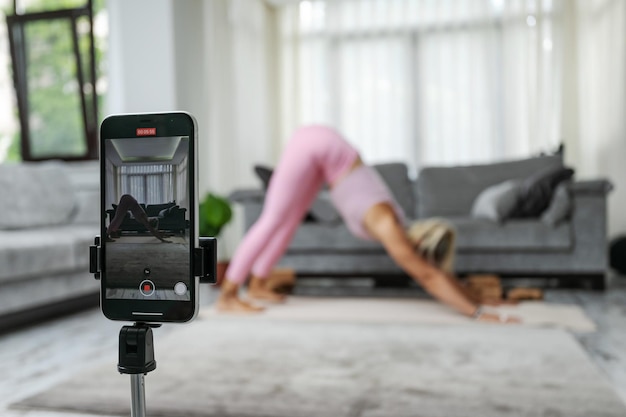 Femme pratiquant des poses de yoga qui s'étend devant la caméra du téléphone blogueur sportif professeur de yoga en ligne