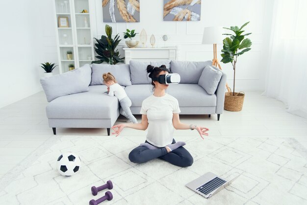 Femme pratiquant le yoga à l'aide d'un casque de technologie VR au cours en ligne à la maison.