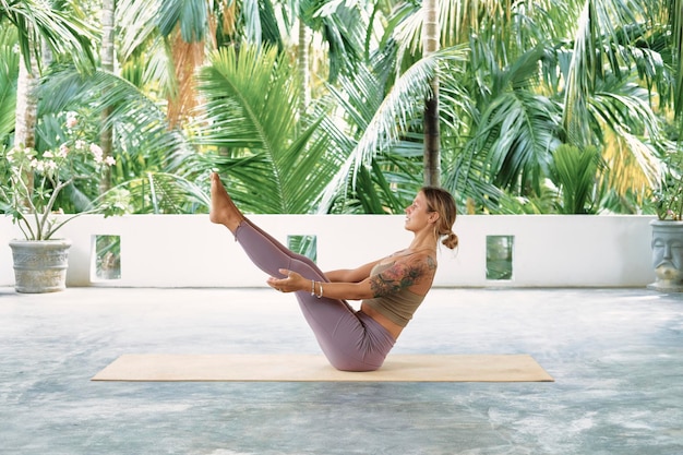 Femme pratiquant le yoga avancé sur tapis organique série de poses de yoga fond tropical