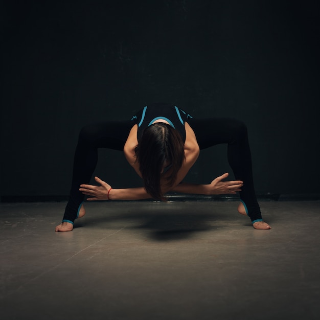 Femme pratiquant le yoga contre un mur sombre texturé