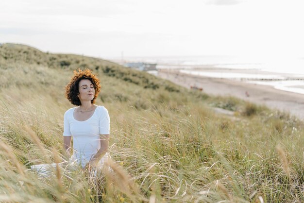 Photo femme pratiquant le yoga dans la dune de la plage