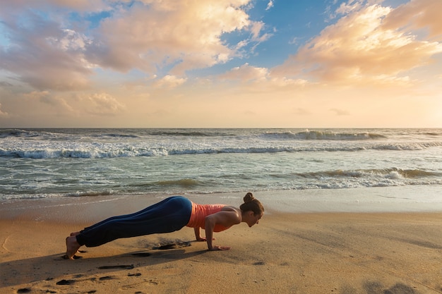 Femme pratique le yoga sur la plage au coucher du soleil