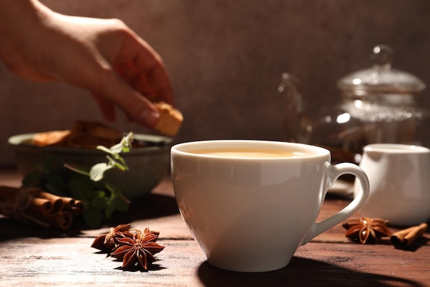 Femme prenant un biscuit dans un bol à une table en bois se concentrant sur une tasse de thé à l'anis avec du lait