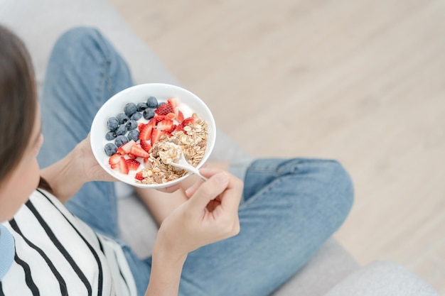 Femme prenant un délicieux petit-déjeuner sain à la maison le matin Une femme de soins de santé mange du yaourt avec du granola et des baies Aliments sains Vitamines régime propre régime désintoxication aliments biologiques végétariens