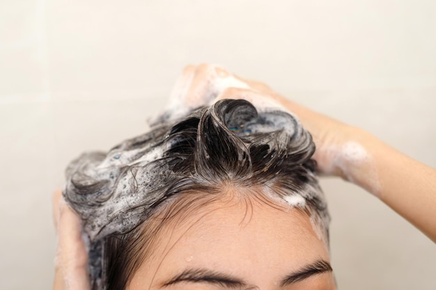 Femme prenant une douche et se lavant les cheveux avec du shampoing dans la salle de bain à la maison