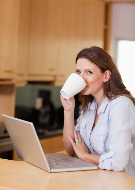 Femme prenant une gorgée de café à côté de l&#39;ordinateur portable