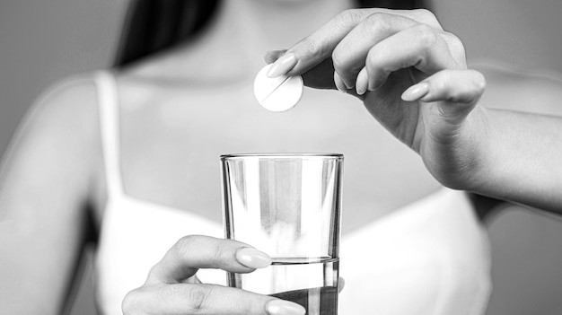 Femme prenant des médicaments pour soulager les maux de tête Prendre des pilules contient un verre d'eau Jeune femme prenant une pilule contre les maux de tête Noir et blanc