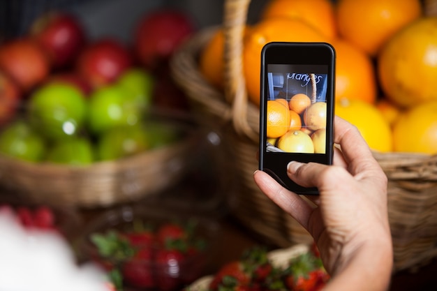 Femme prenant une photo d'oranges sur téléphone mobile dans la section organique