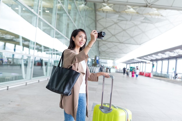 Femme prenant une photo par caméra avec ses bagages à l'aéroport