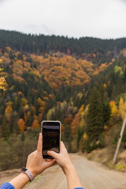Photo femme prenant une photo sur son smartphone des couleurs d'automne de la montagne et de la forêt d'automne