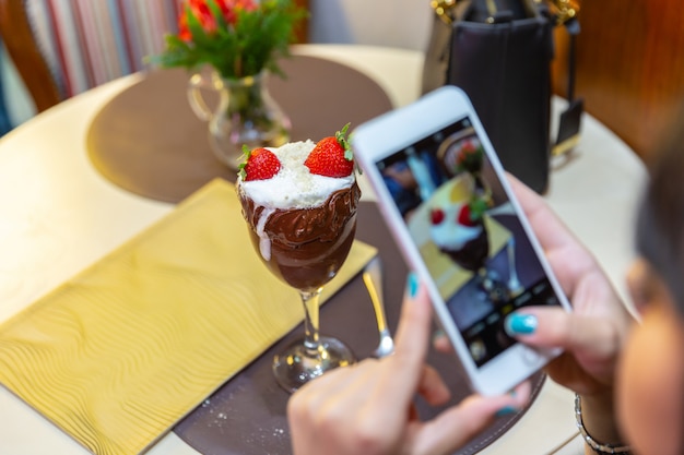 Femme prenant des photos de la crème glacée délicieuse mélange blanc fraise avec un téléphone intelligent.