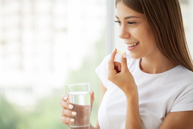 Femme prenant une pilule avec de l'huile de foie de morue oméga et tenant un verre d'eau fraîche le matin