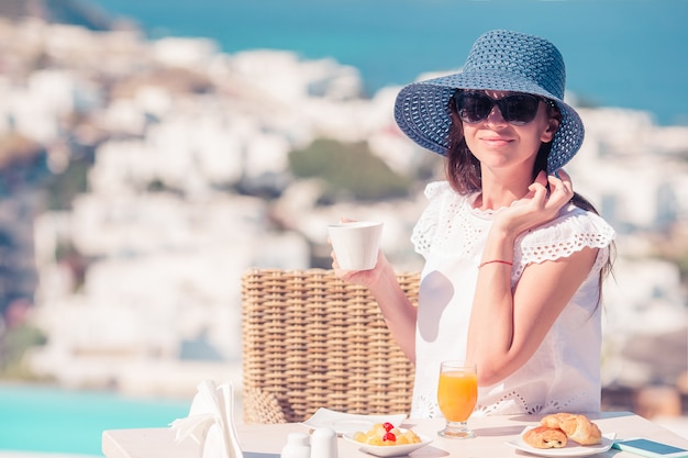 Femme prenant son petit déjeuner au café en plein air avec vue imprenable sur la ville de Mykonos.