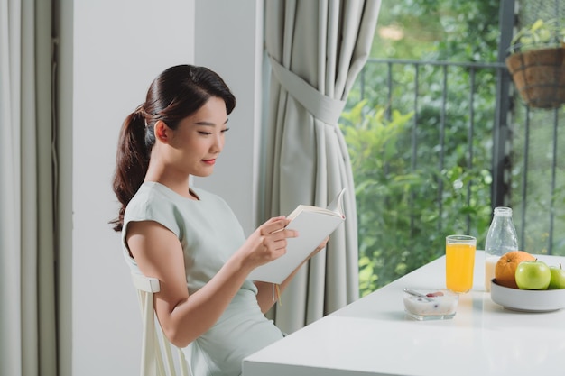 Femme prenant son petit déjeuner et lisant un livre à la maison