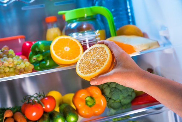 La femme prend l'orange du réfrigérateur ouvert. Nourriture saine.