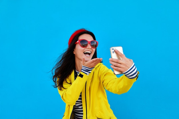 Femme prend photo autoportrait bonnet tricoté fond bleu smartphone