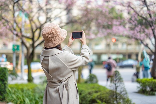 Une femme prend une photo d'une fleur de sakura sur son téléphone portable