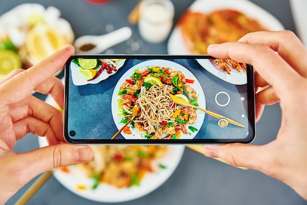 Une femme prend une photo de nourriture avec un smartphone pour les médias sociaux, une caméra de téléphone prend une photo de nouilles sautées au wok avec des crevettes