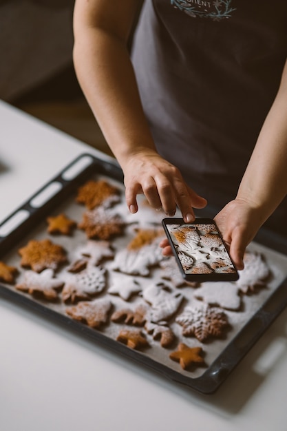 La femme prend la photo sur le pain d'épice de Noël de smartphone saupoudré de sucre en poudre