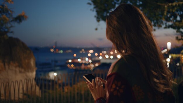 Une femme prend une photo panoramique de la ville du crépuscule depuis le pont d'observation du parc.