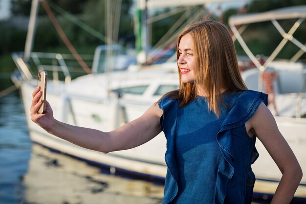 Photo une femme prend une photo selfie sur son smartphone alors qu'elle se tient sur le port de plaisance de la rivière