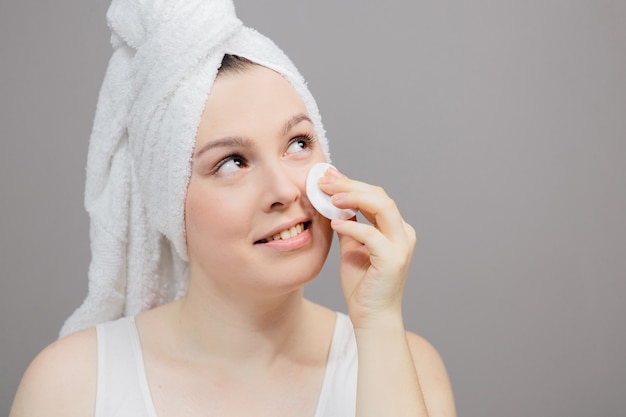 femme prend soin de son visage, après une douche dans une serviette sur un gris, un coton à la main