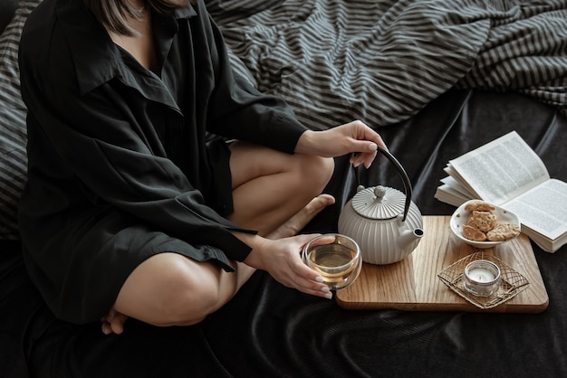 Une femme prend son petit déjeuner avec du thé et des biscuits, allongée dans son lit un jour de congé.