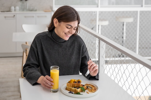 Une femme prend son petit déjeuner avec des gaufres belges et du jus d'orange.