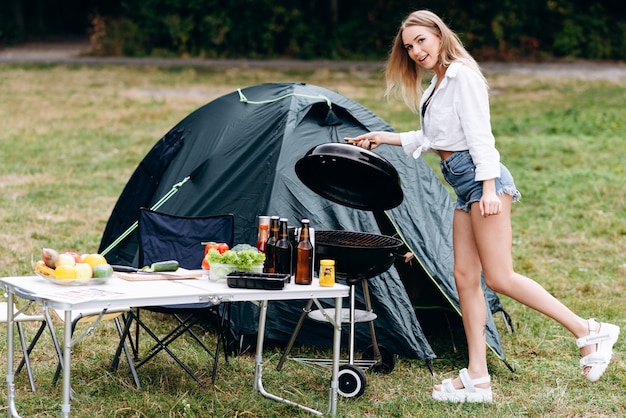 Femme préparant la nourriture sur le barbecue en plein air dans le camping et en regardant la caméra