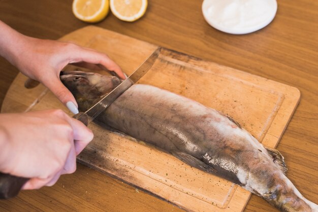 Une femme prépare du poisson, couper du poisson sur une planche de bois, le cuisinier assaisonne la truite