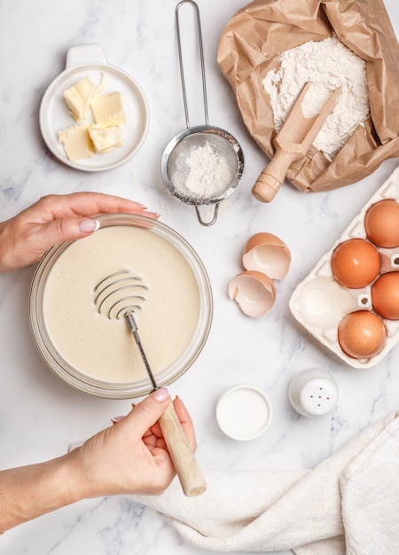 Femme prépare la pâte pour les crêpes faites maison pour le petit déjeuner, fouet pour fouetter dans les mains