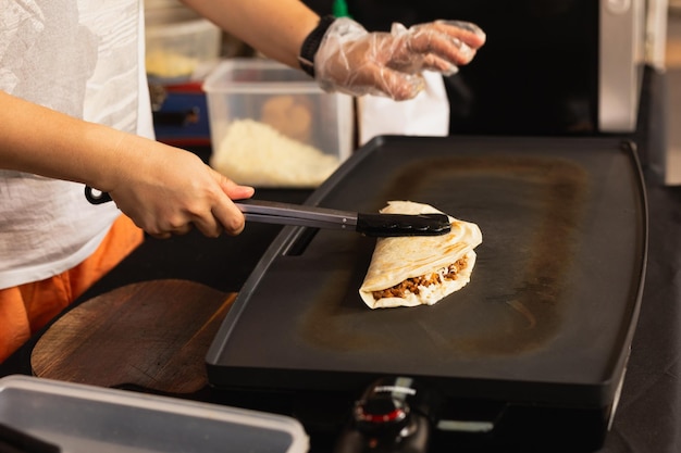 Une femme prépare de la quesadilla fraîche sur un gril noir au marché alimentaire local