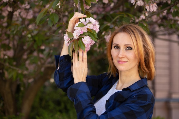 Femme près de sakura arbre en fleurs Fleurs roses concept de printemps et de jeunesse Fille élégante souriante