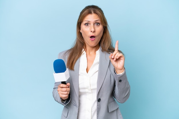 Femme présentatrice de télévision d'âge moyen sur fond bleu isolé ayant l'intention de réaliser la solution tout en levant un doigt