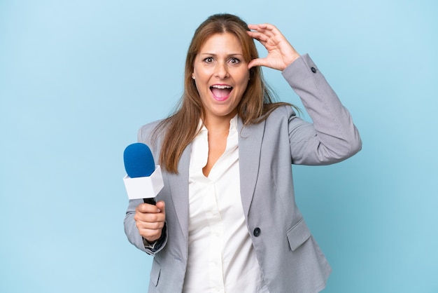 Femme de présentatrice de télévision d'âge moyen sur fond bleu isolé avec une expression de surprise