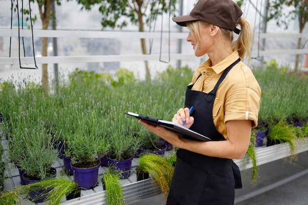 Femme avec presse-papiers vérifiant la qualité des fleurs dans une serre