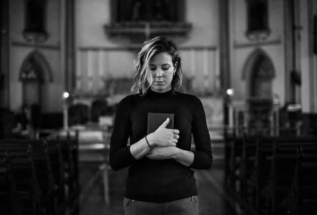 Photo femme priant dans l'église en niveaux de gris