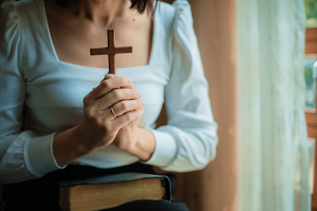 femme prie avec bible et croix en bois.