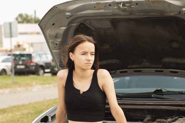La femme à problème de voiture avec une voiture cassée sur la route est triste avec un capot ouvert attendant de l'aide